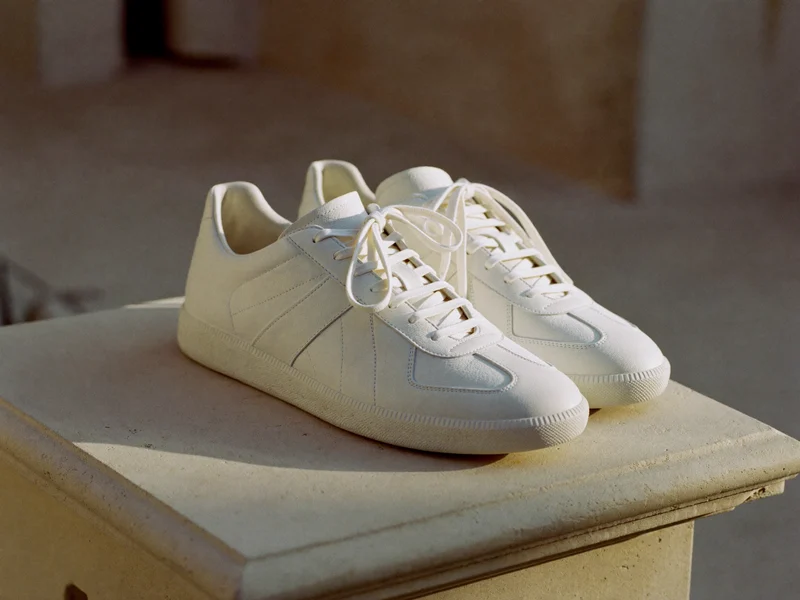 Weiße Leder-Sneaker schräg von vorn auf einem hellen Steinblock